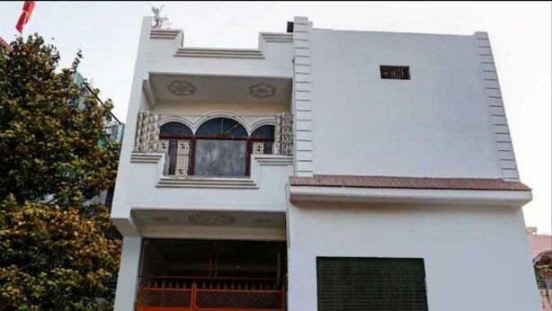 A building with a flat roof, a large window with decorative elements, and a closed orange gate. - Hotel O Sant Ravidas Ghat Varanasi (Varanasi)