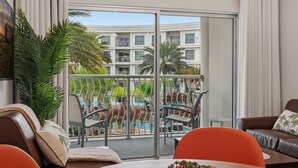 Un balcone con vista su una piscina e un edificio. Sono presenti sedie, un tavolo e un vaso di fiori.