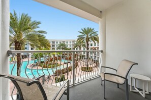Ein Balkon mit Blick auf einen Swimmingpool, Palmen und ein Gebäude im Hintergrund.