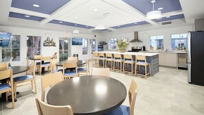 Un comedor moderno con mesas y sillas redondas, una cocina con una isla central y ventanas amplias que ofrecen vistas.