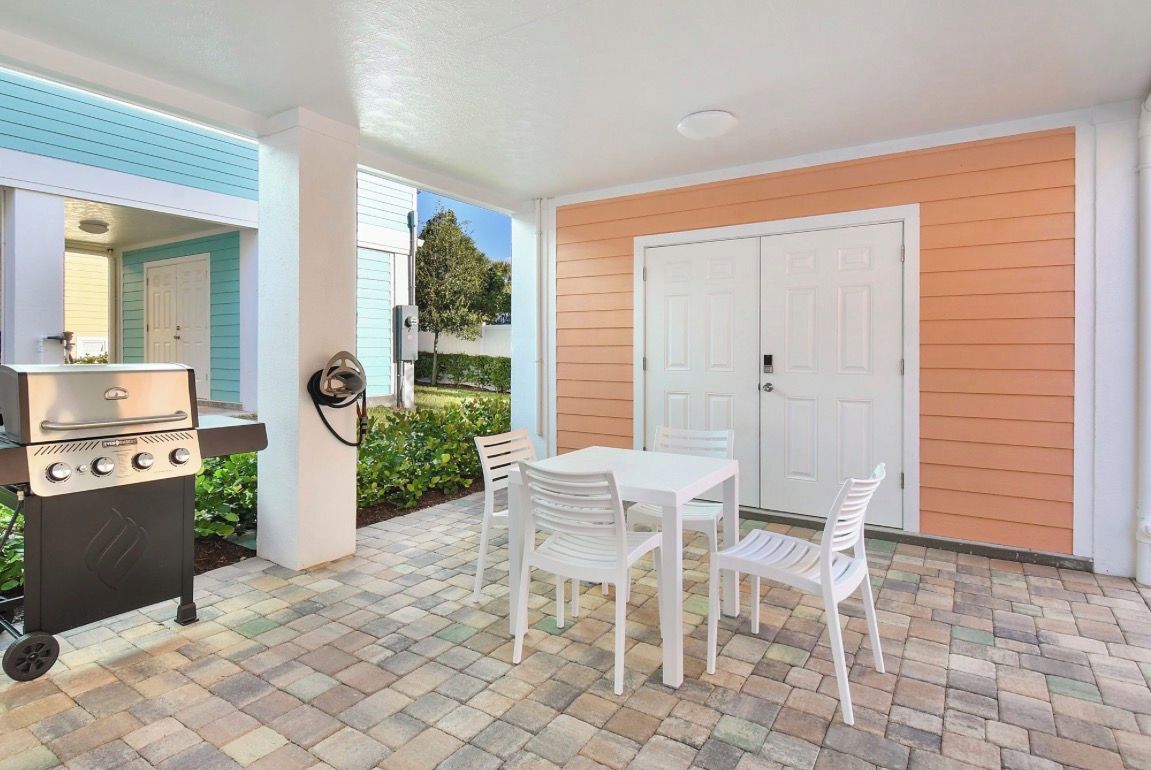 An outdoor patio with a grill, white table and chairs, and a door.