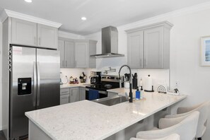 A modern kitchen with stainless steel appliances, a central island, and grey cabinetry. - Coastal Retreat: Pool, Kayak, Beaches & Bikes (Jensen Beach)