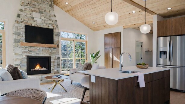 A modern kitchen with a stone fireplace, wooden ceiling, and a large island with a sink. - Refined Mountain Cabin on Pisgah Trails (Old Fort)