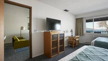 A hotel room with a bed, a television, a wooden cabinet, a desk with a chair, and a view of the outdoors.