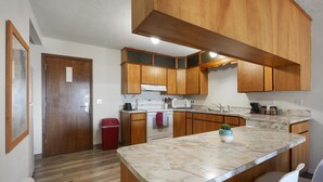 Una cocina con armarios de madera, encimera de mármol, un bote de basura rojo y una pequeña planta en maceta.