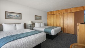 Una habitación de hotel con dos camas, un armario, una lámpara y dos cuadros en la pared.
