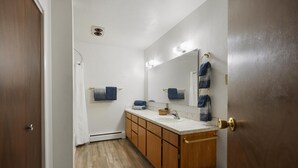 Un baño con armarios de madera, un lavamanos blanco, un espejo con iluminación y un perchero para toallas.