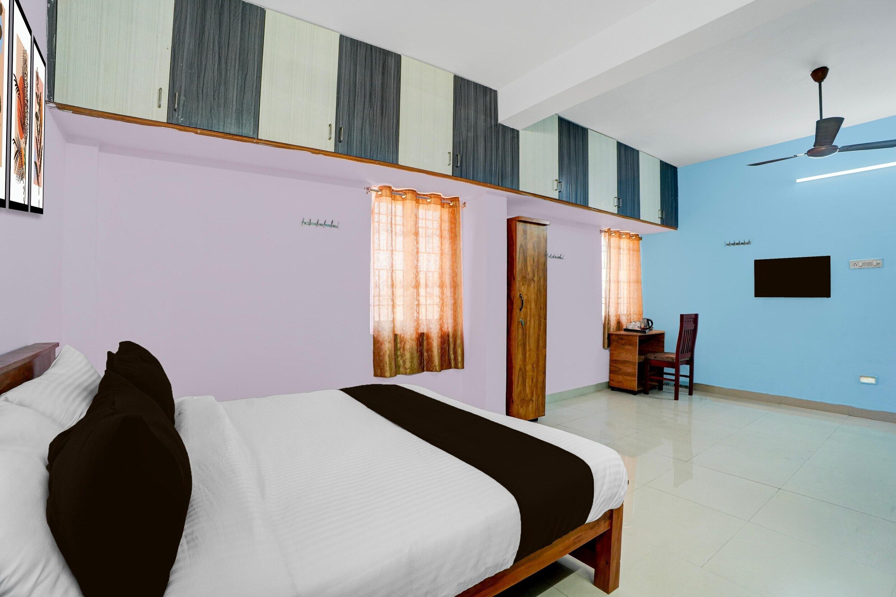 A bedroom with a bed, a desk, a chair, a ceiling fan, and a TV.