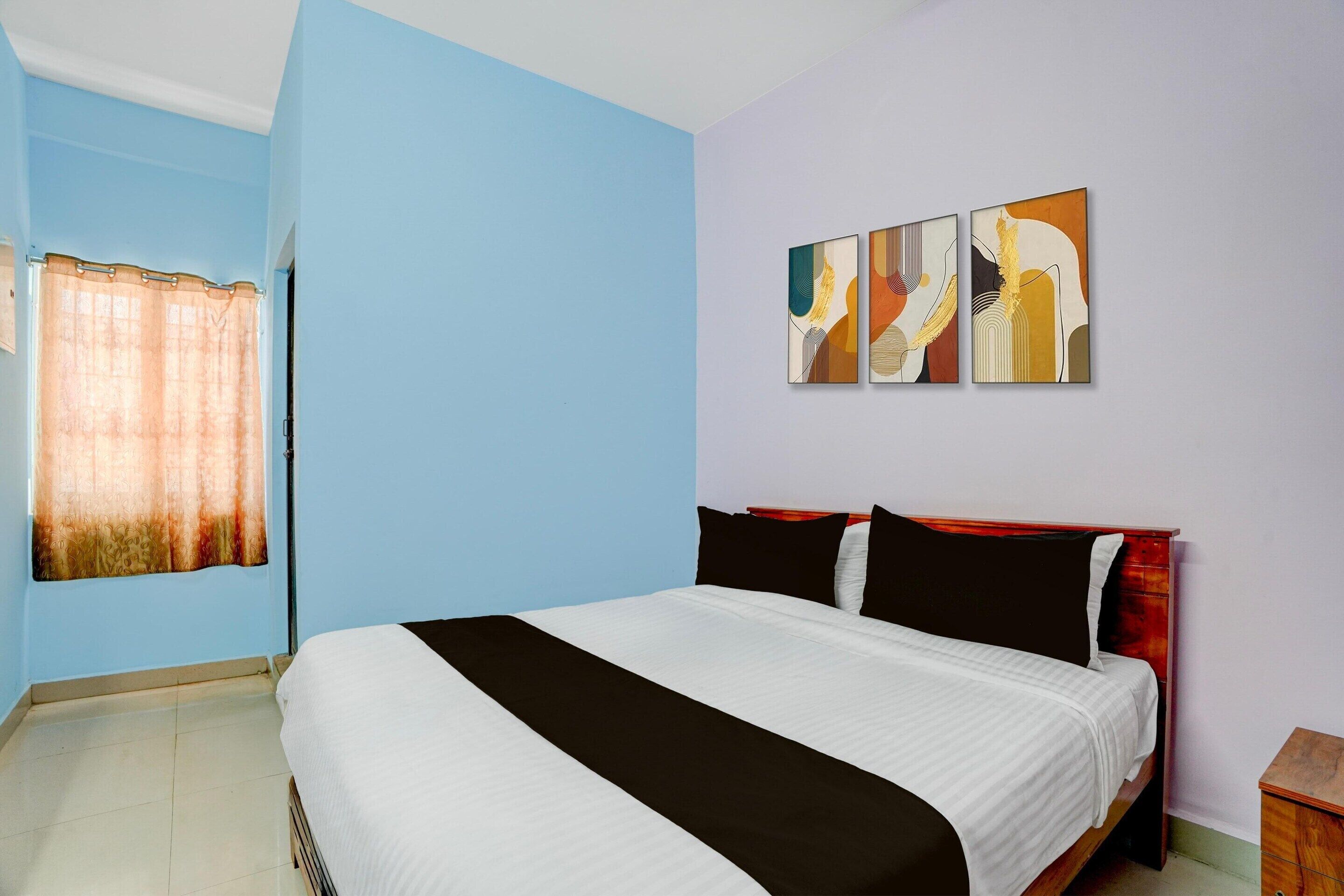 A bedroom with a bed, a window with curtains, and three wall-mounted paintings.