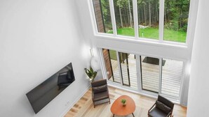 Una sala de estar moderna con un ventanal grande, un televisor de pantalla plana, dos sillones y una mesita.