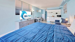 Una camera d'albergo moderna con un letto grande, una scrivania, una sedia, angolo cottura e una TV che mostra 'BIG FISH Rentals'.