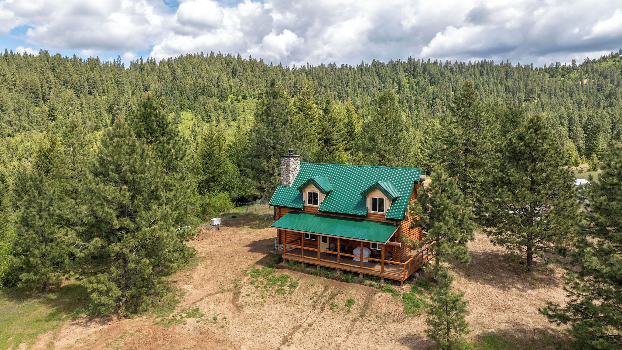 Une cabane en rondins surmontée d’un toit végétalisé, entourée d’une forêt dense.