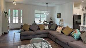 A living room with a sectional sofa, a glass coffee table, and a dining area with a table and chairs.