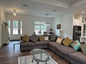 Una sala de estar con un sofá modular, una mesa de centro de vidrio y un comedor con mesa y sillas.