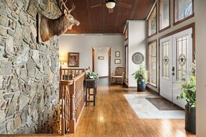 A stone wall with a mounted deer head, wooden railing, and a staircase leading to upper floors.