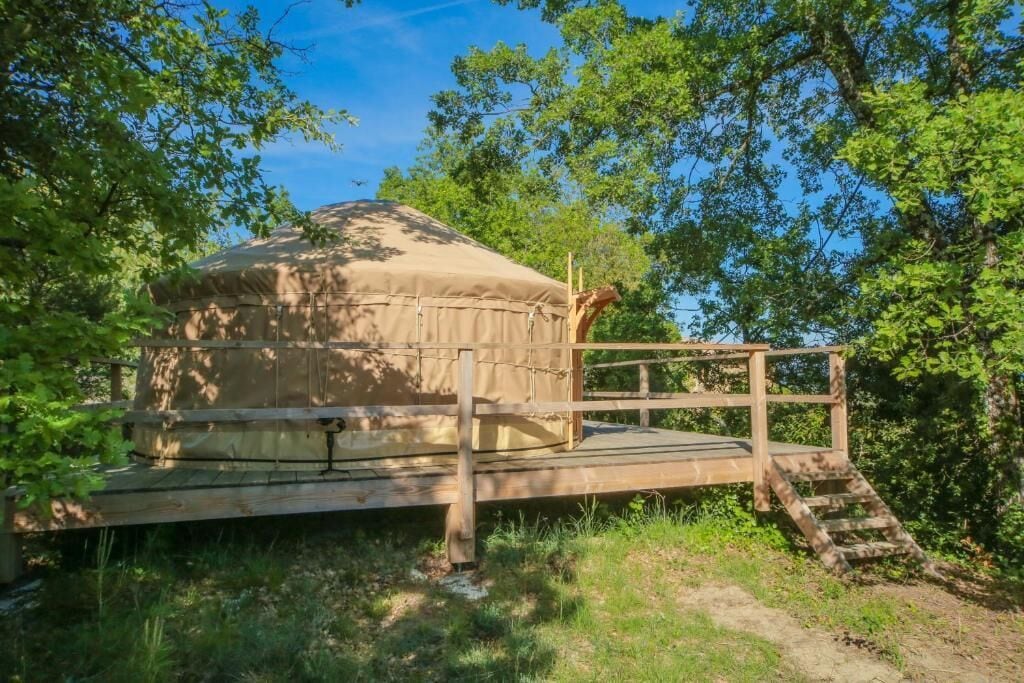Een houten terras met overdekte constructie, omringd door bomen.