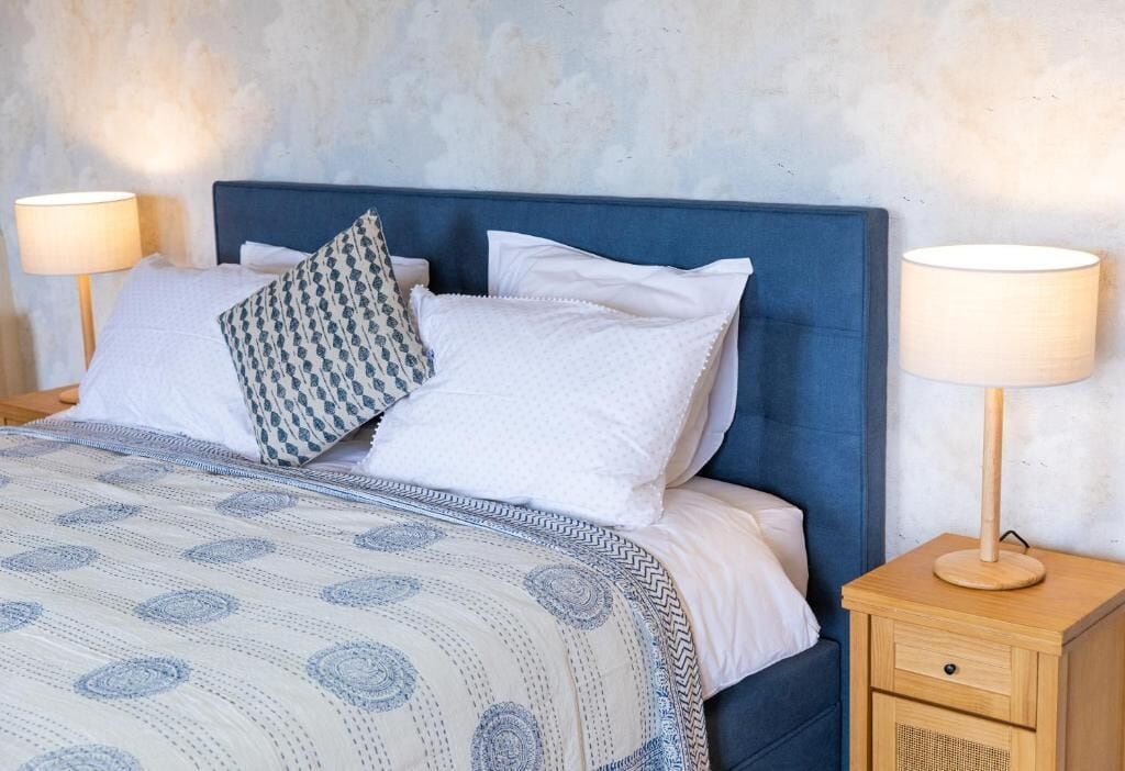 A neatly made bed with a patterned bedspread, a blue headboard, and two bedside lamps on wooden nightstands.