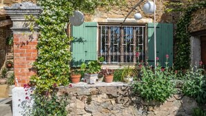 A rustic stone building with a green shuttered window, potted plants, and hanging lanterns. - Les Yourtes de Provence (Saint-Paulet-de-Caisson)