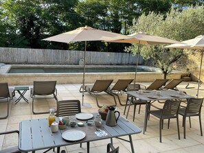 Une terrasse extérieure avec des tables et des chaises, une piscine et des parasols.