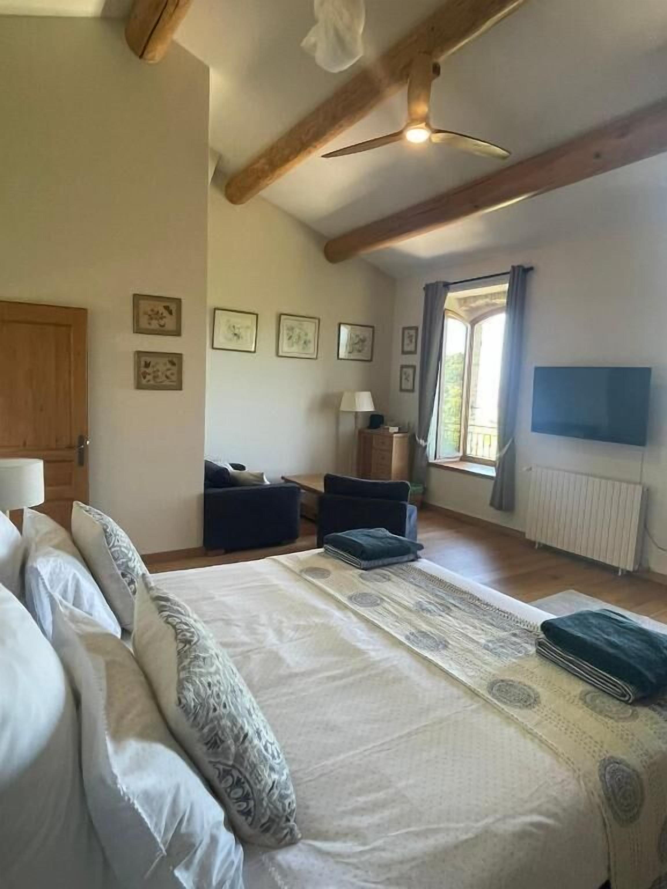 A bedroom with a large bed, a desk, a chair, a TV, and a window with curtains.