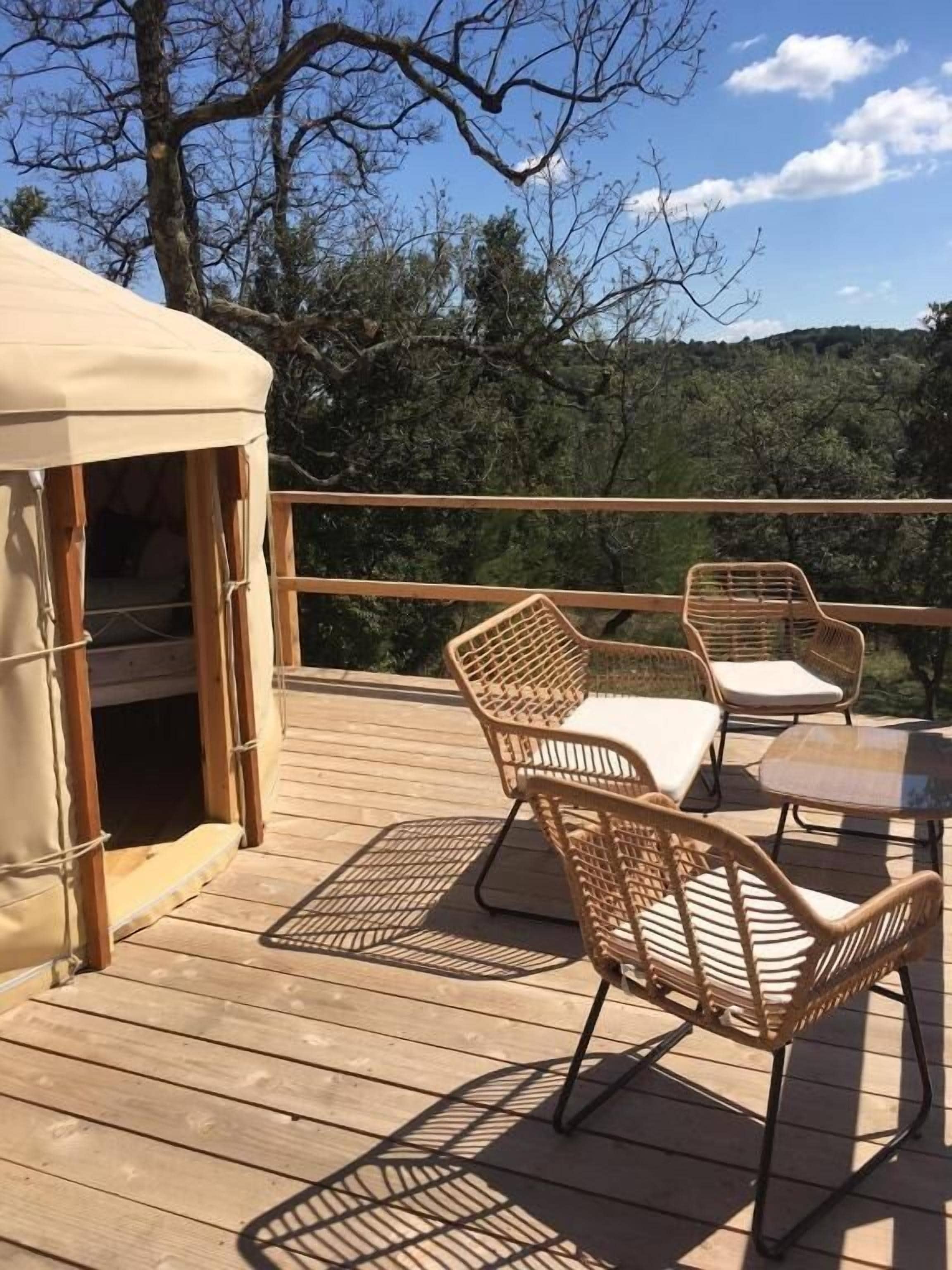 Une terrasse en bois, dotée de meubles en osier et d’un espace abrité, qui offre une vue sur un paysage boisé.