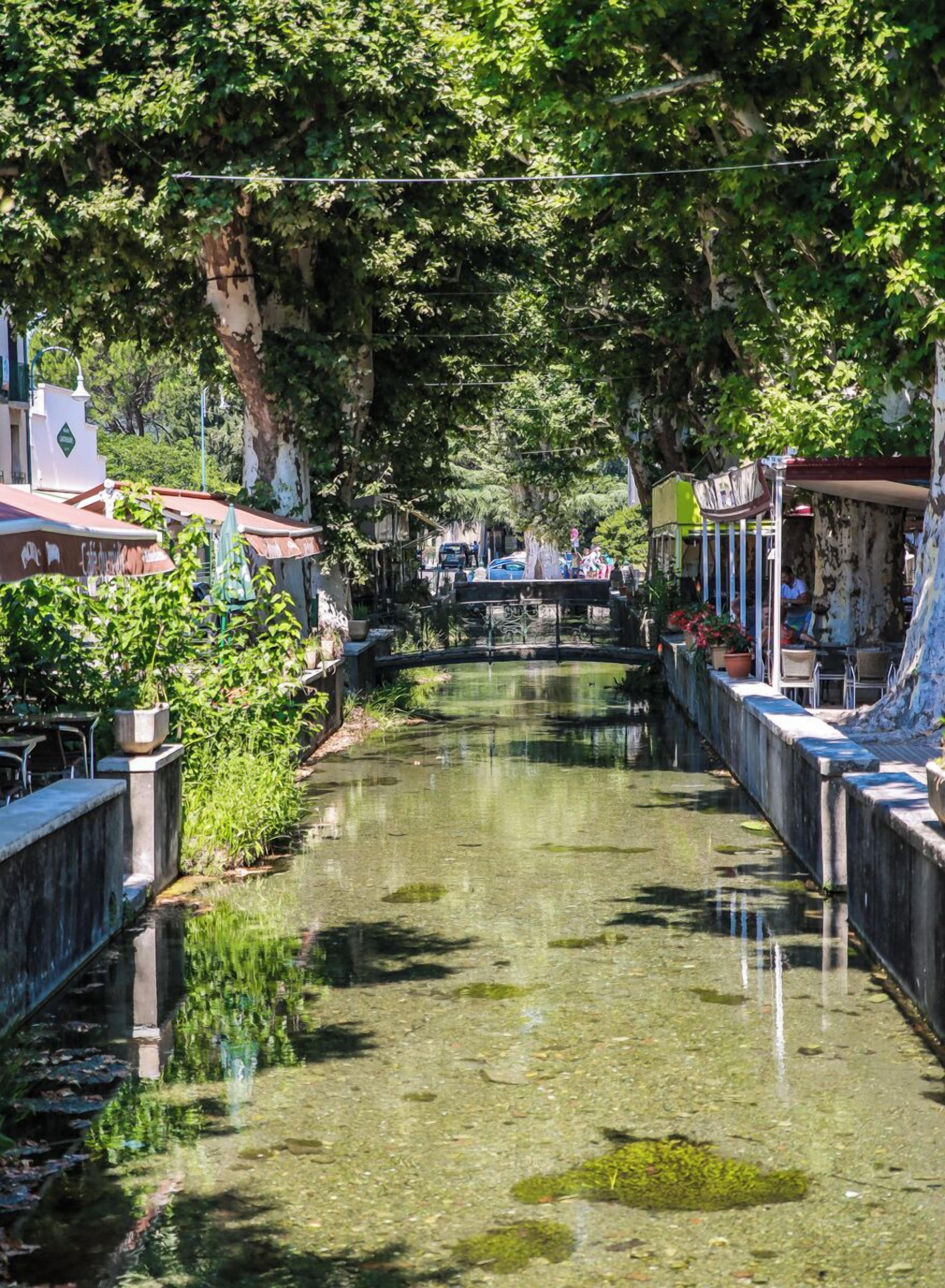 Un cours d’eau étroit bordé d’immeubles, d’un pont et d’une végétation luxuriante.