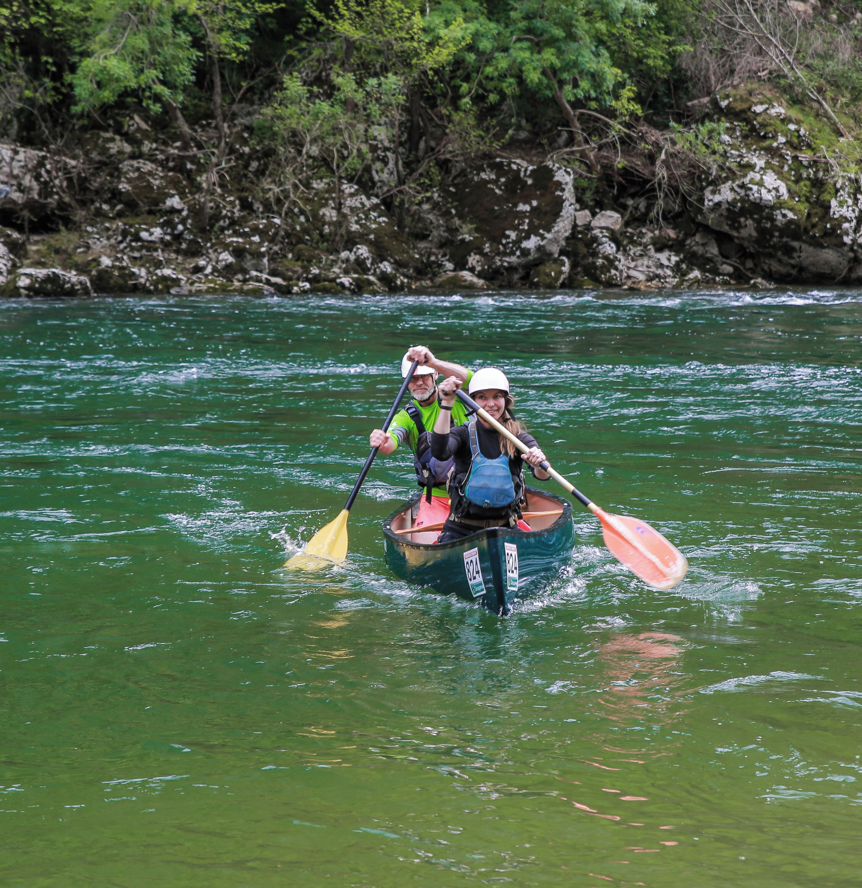 Dos personas kayakendo en un río rodeado de terreno rocoso y vegetación.