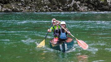 Dos personas kayakendo en un río rodeado de terreno rocoso y vegetación.