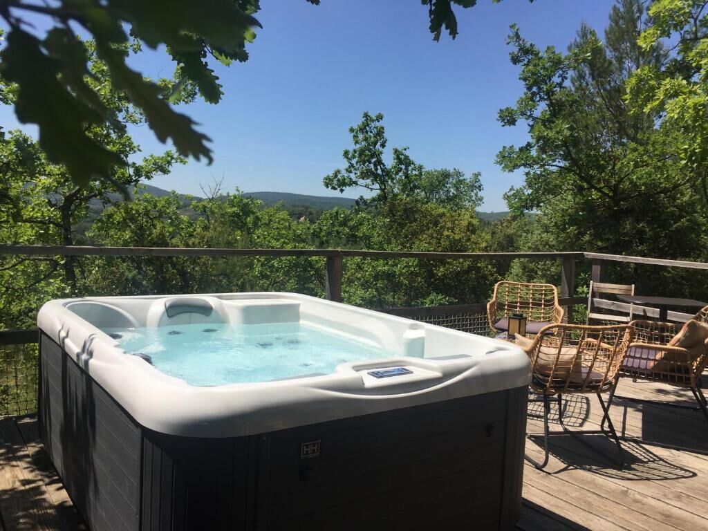 A hot tub on a wooden deck with wicker chairs and a view of trees and hills.