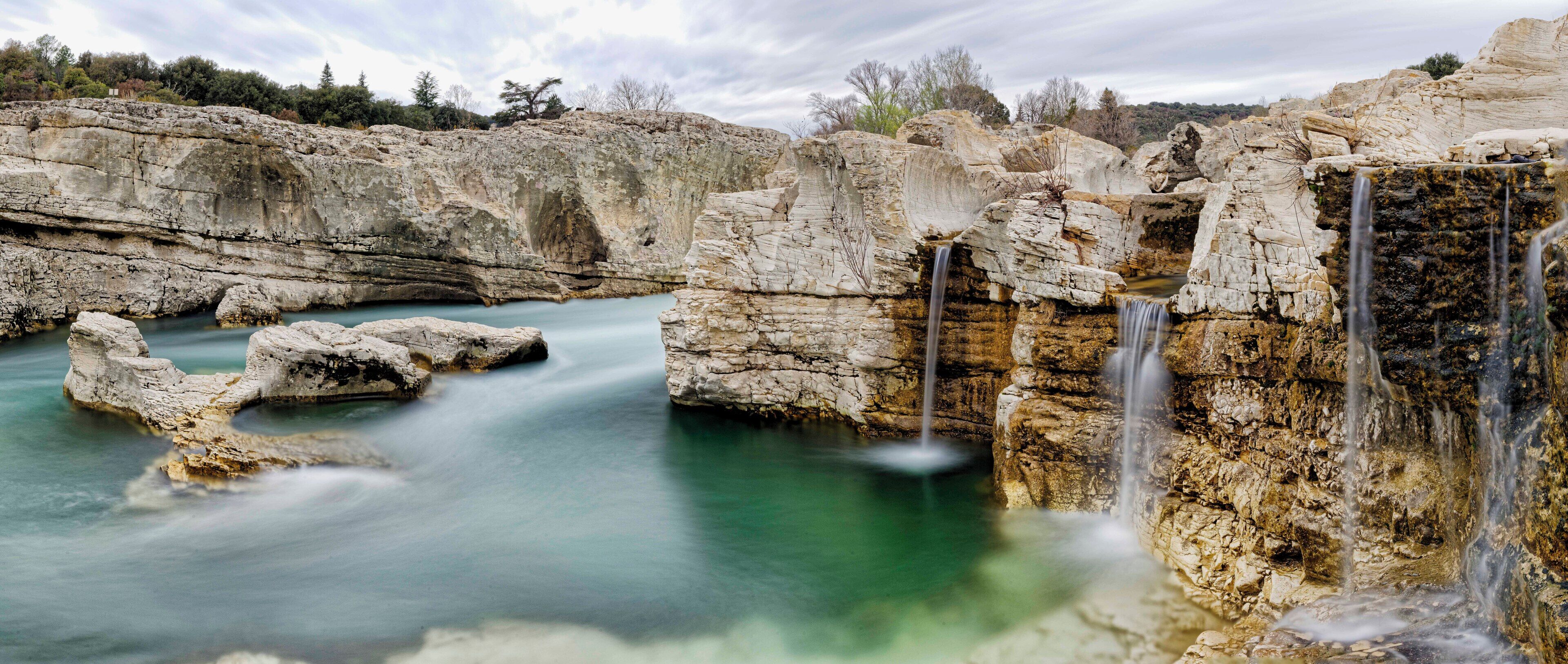 Un paysage naturel comprenant une cascade, des formations rocheuses et un bassin d’eau limpide.