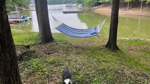 A hammock between trees overlooking a calm lake with boats and a dock in the background. - The Shamrock Lake Norman. Swim, fish, kayak, boating, pool, hot tub, jet ski. (Statesville)