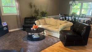 A living room with a sofa, a coffee table, and a dining table with chairs. - The Shamrock Lake Norman. Swim, fish, kayak, boating, pool, hot tub, jet ski. (Statesville)