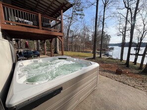 Een hottub met een houten terras en uitzicht op een meer.