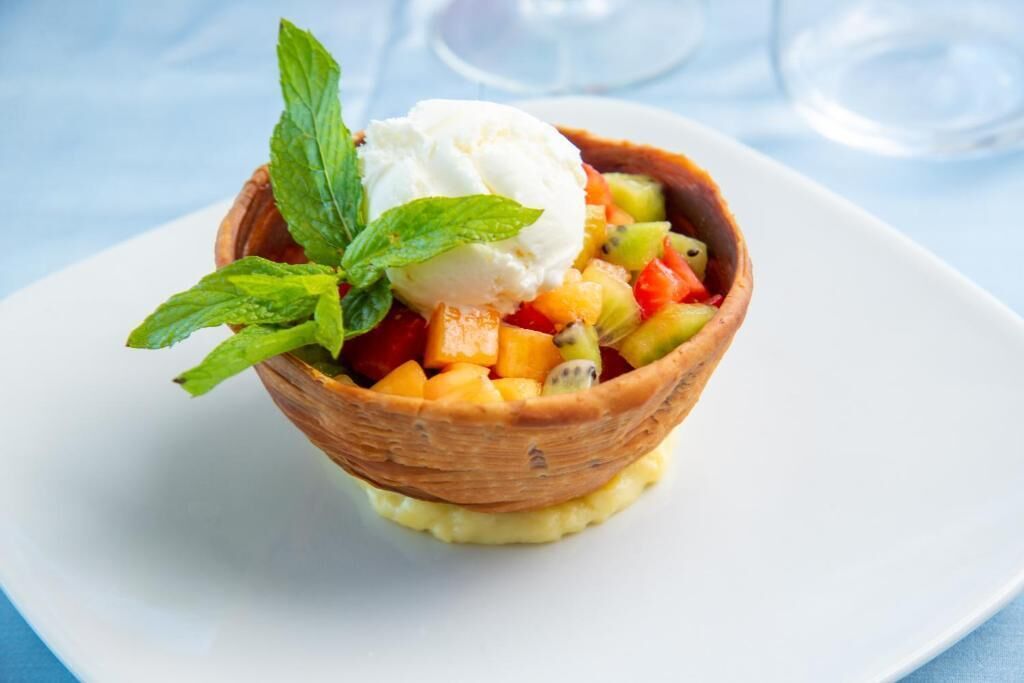 A dessert in a bowl with fruit and a scoop of ice cream, garnished with mint leaves.