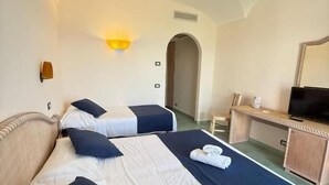 A hotel room with two beds, a desk, a television, and a wall-mounted light fixture.