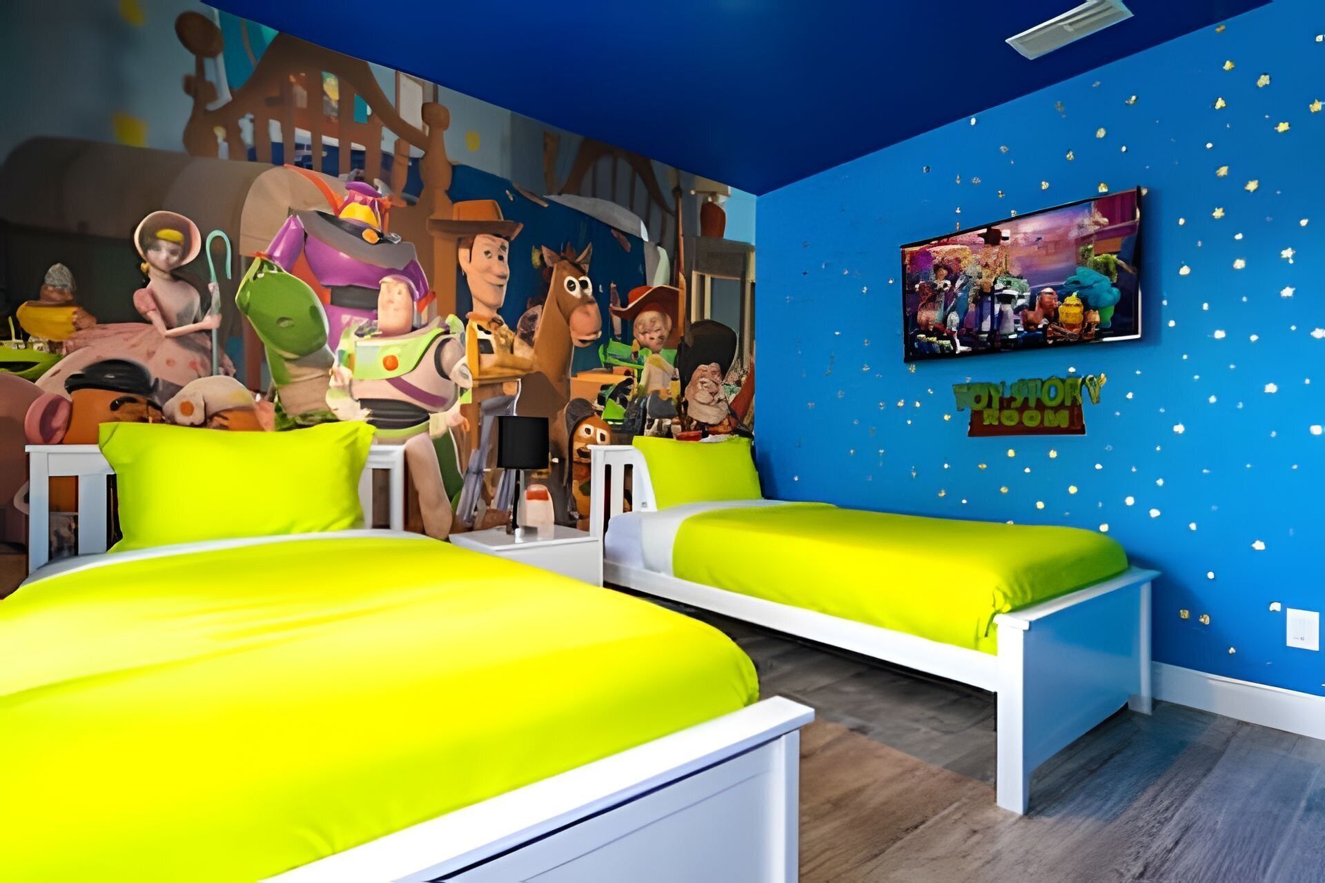 A children's room with two beds, a mural of animated characters, and a TV on the wall.