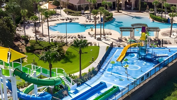 Parque acuático con múltiples toboganes y piscinas, rodeado de zonas ajardinadas y edificios.