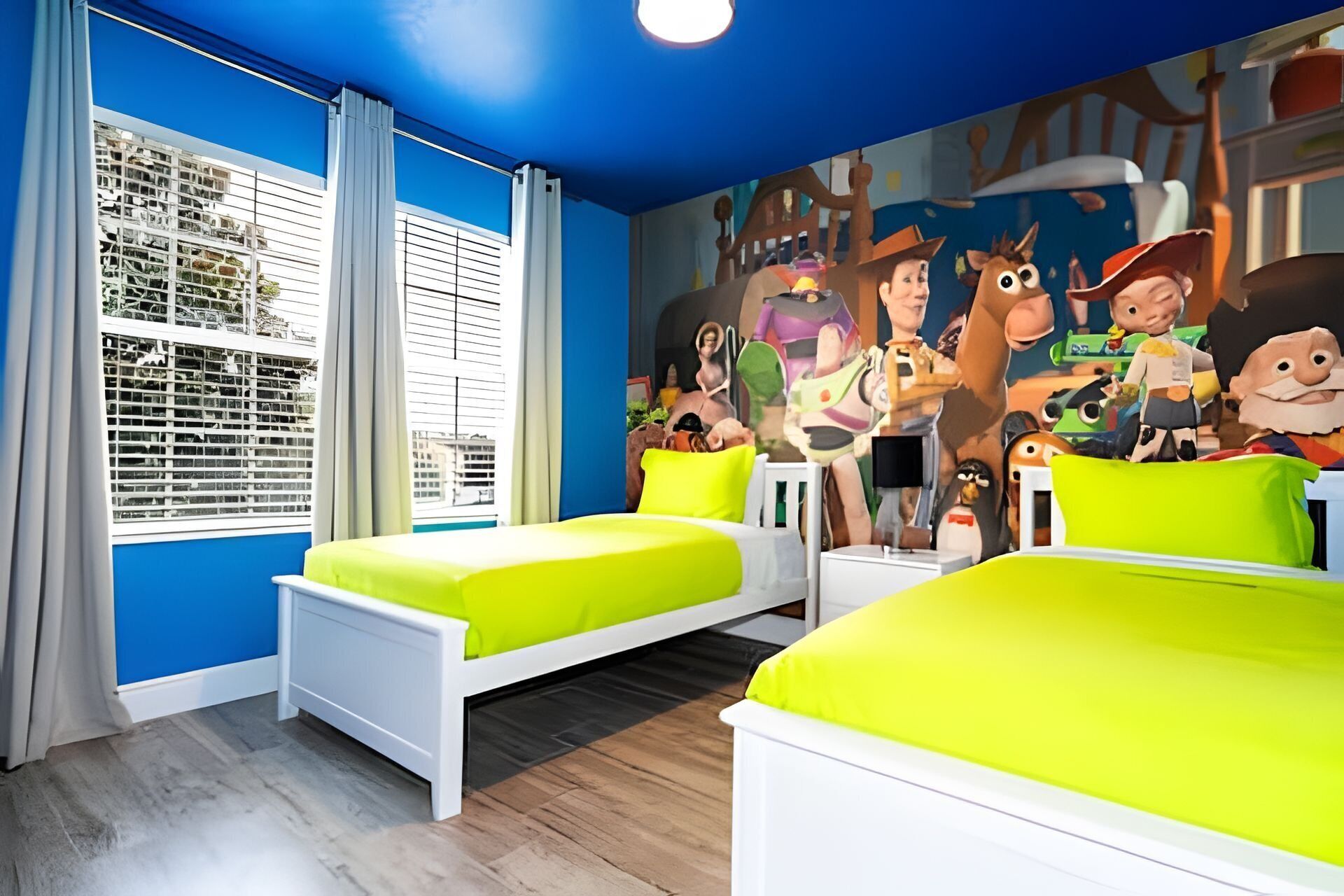 A room with two beds, a large window with blinds, and a colorful mural on the wall.