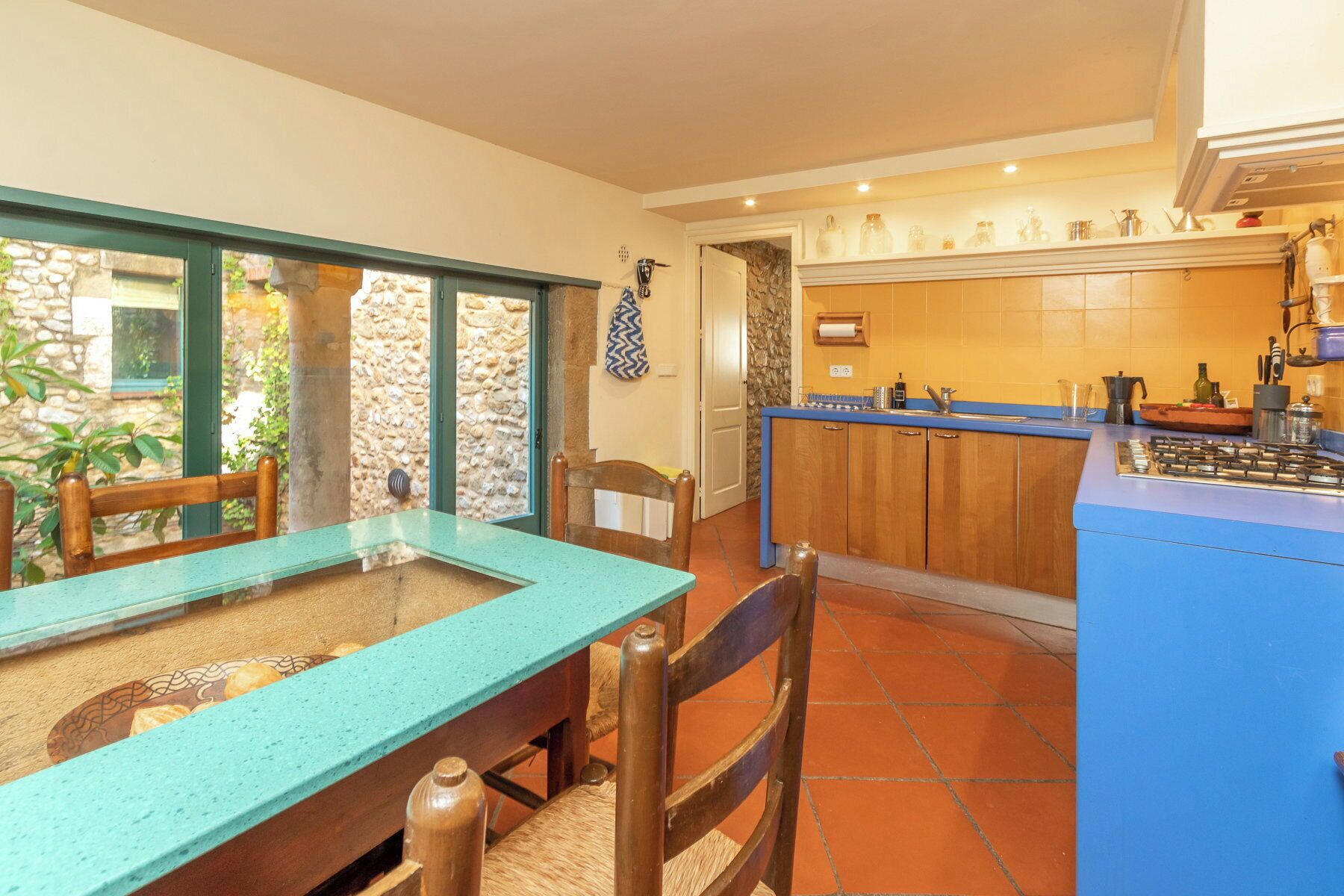 A kitchen with a blue countertop, wooden cabinets, and a stone wall.