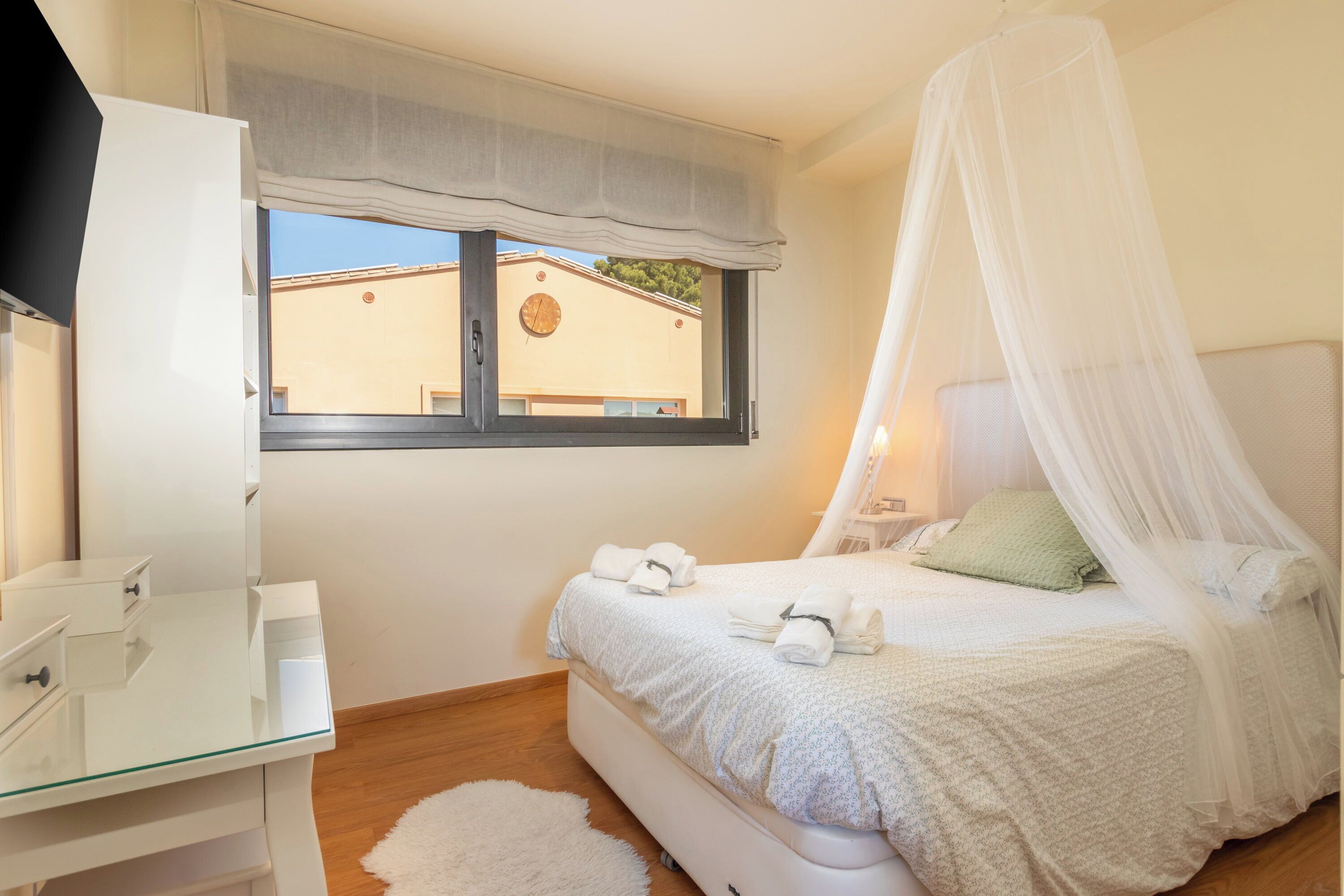 A bedroom with a bed, a bedside table, a mirror, a window with a view, and a canopy bed.
