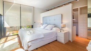 Ein modernes Schlafzimmer mit einem großen Bett, einem begehbaren Kleiderschrank und Blick ins Freie.