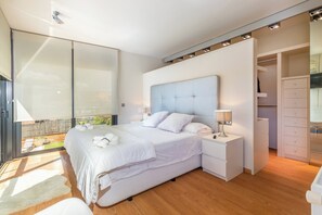 Ein modernes Schlafzimmer mit einem großen Bett, einem begehbaren Kleiderschrank und Blick ins Freie.