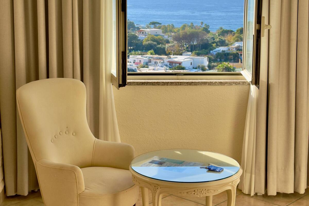 Une pièce avec vue sur la mer, un fauteuil beige et une petite table avec un magazine.