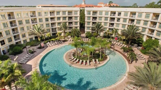A hotel with a circular pool surrounded by palm trees and lounge chairs. - Orlando Getaway With Pool View Balcony (Celebration)