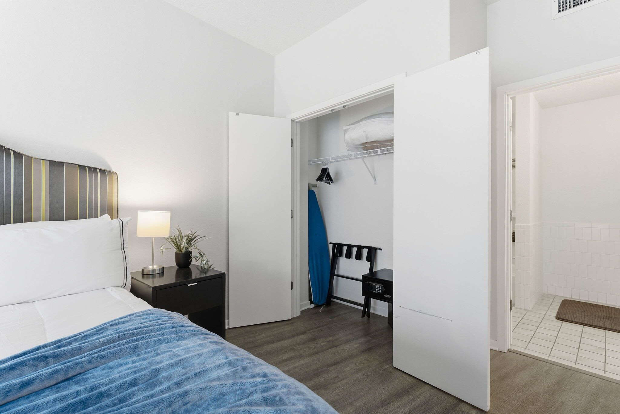 Ein Hotelzimmer mit Bett, Nachttisch, Lampe und einem Schrank mit Kleidung.