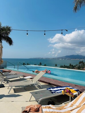 Zona de piscina amb gandules, piscina i vista a l'oceà i a les muntanyes.
