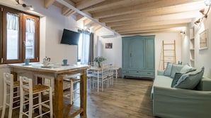 A cozy room with a wooden ceiling, a dining area with white chairs, a light blue cabinet, and a sofa. - GuestHost - Comfortable mezzanine apartment of approximately 35 square meters, accommodating up to four people, located on the first floor of a building without an elevator.The property is located in Visgnola, a quiet hamlet of Bellagio, one of Lake Como (Bellagio)