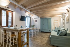 Une pièce chaleureuse avec un plafond en bois, un coin repas avec des chaises blanches, un meuble bleu clair et un canapé.
