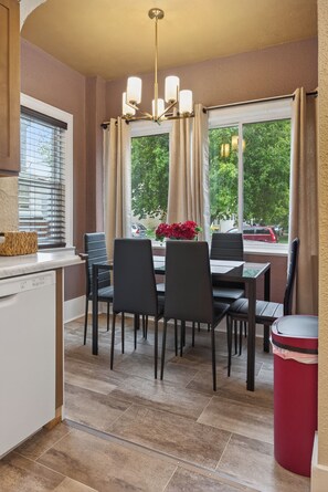 Un espace repas comprenant une table, des chaises, un lustre et une fenêtre avec des rideaux.
