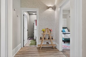A hallway with a wooden ladder shelf holding decorative items, a patterned wall, and a bed in the background. - Westside 4 Bedroom 2 Bath Furnished Remodeled. Close to Bridge St GR City. (Grand Rapids)